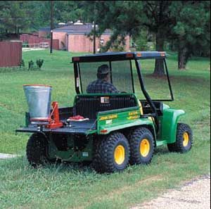 Man applying fire ant treatment with spreader attached to the back of a Gator utility vehicle.