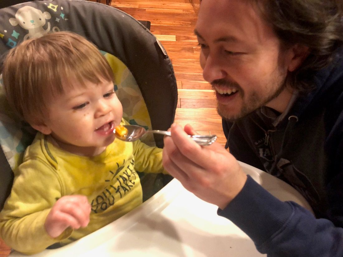 A father feeding his son baby food. 
