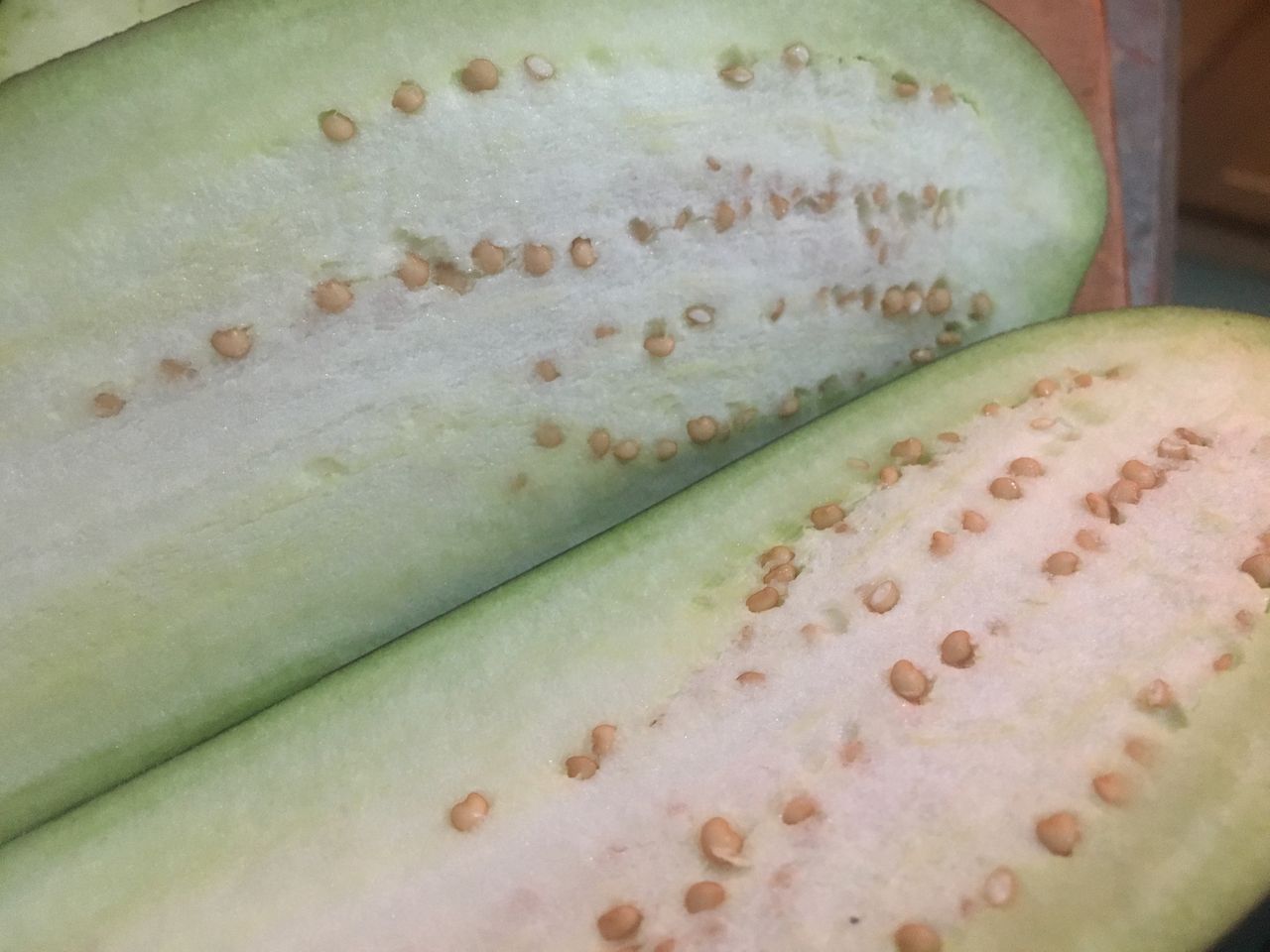 Close-up image shows two halves of a mature eggplant cut from top to bottom; inside the halves, the surface is solid and white to pale yellow-green in color with a few straight lines of small round golden yellow arranged from top to bottom.