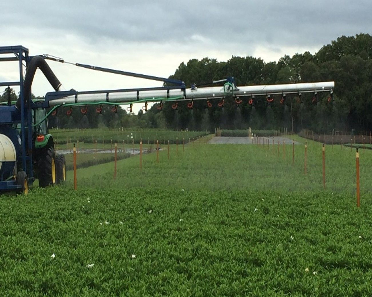 Tracker moves over grass as it sprays a liquid from many nozzles dangling at the underside of a high-hanging, metal arm-like attachment.