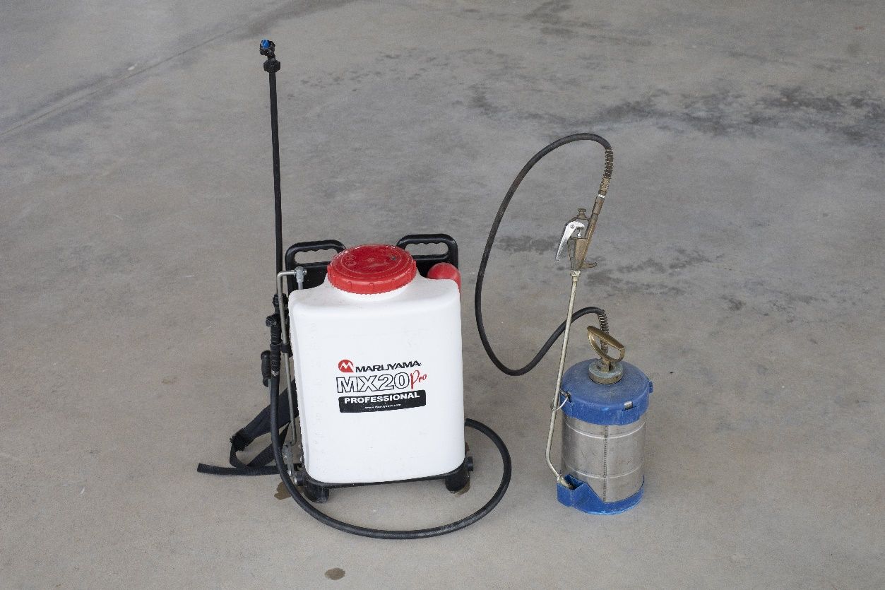 On the left is a medium-sized container with lid that can be held as a backpack and has a skinny hose attached from the bottom of the container to a metal rod with nozzle; on the right is a small cylindrical canister with a skinny hose attached from the top near a handle to a metal rod with nozzle.