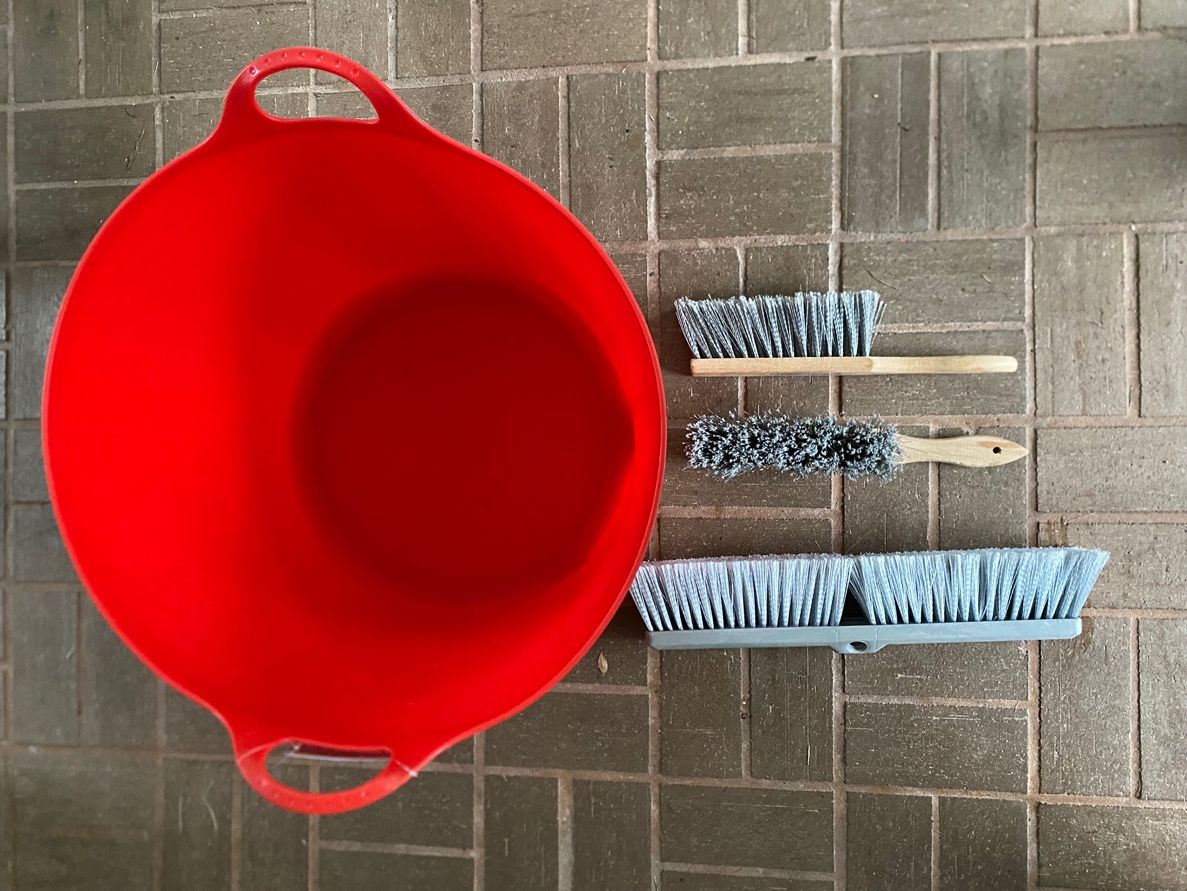 A flexible plastic tub with handles, and brushes on a tile floor.
