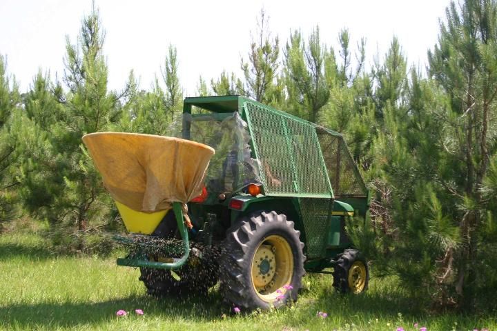 Figure 2. Mineral fertilizer application with a centrifugal fertilizer spreader. Note the cage on the tractor and the cover on the spreader, especially useful in younger stands.