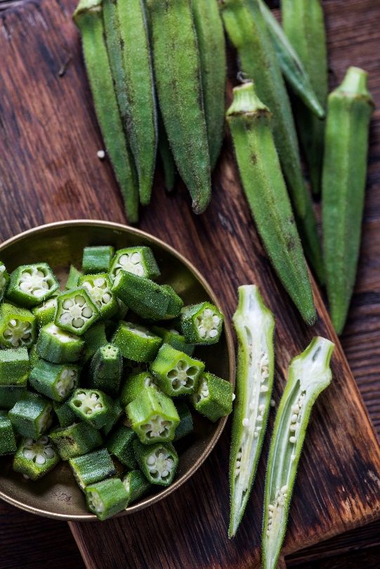 A bowl of chopped okra next to halved and whole okra pods