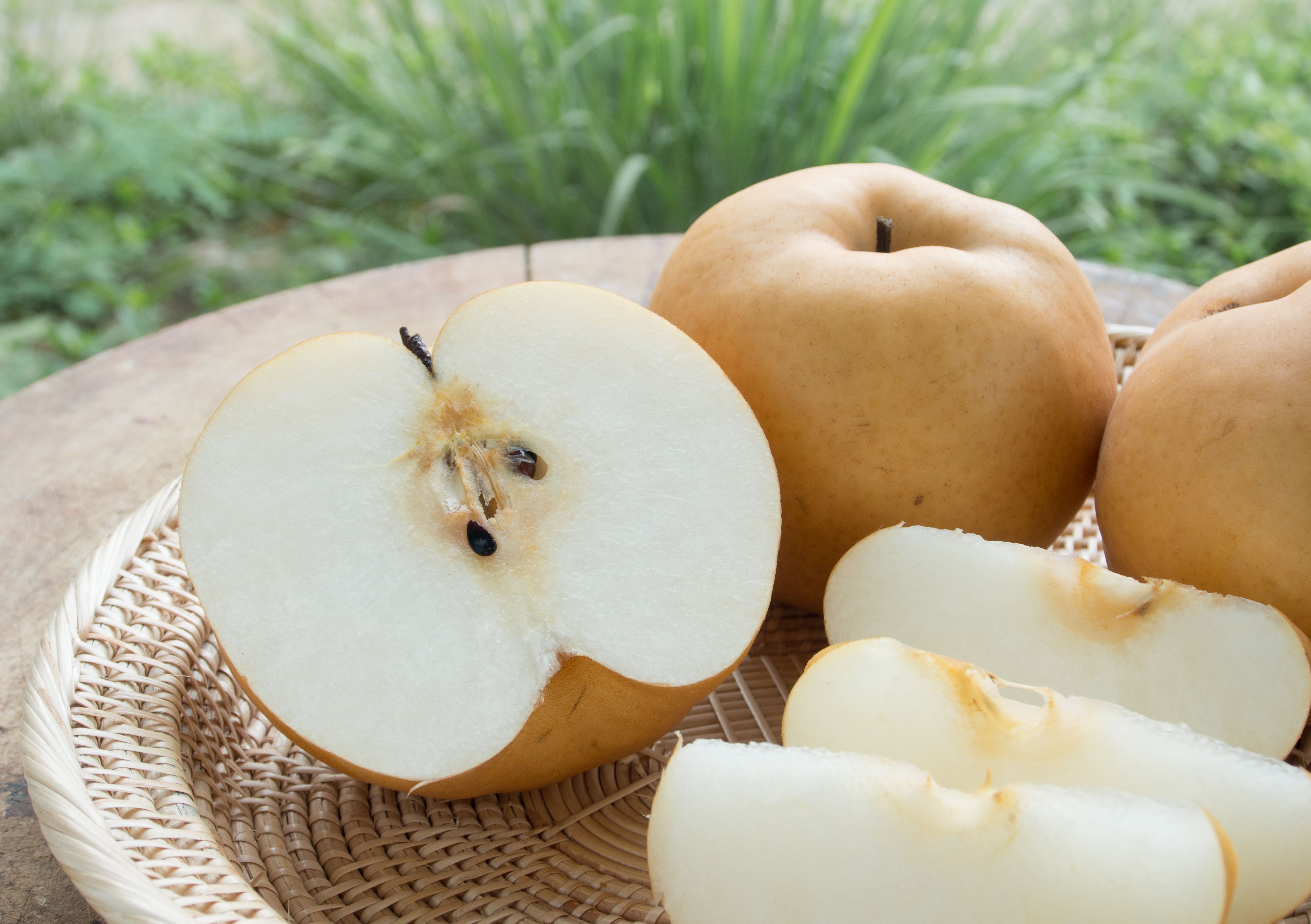 An Asian pear sliced in half next to some pear silces and whole pears.