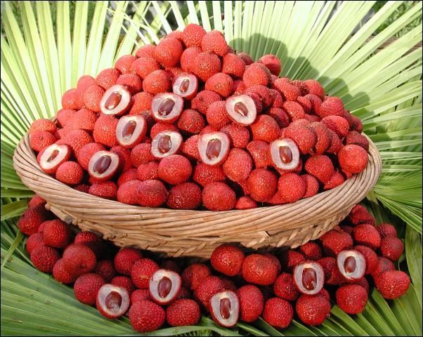 Cesta colmada de muchas frutas de lichi de color rojo intenso, algunas están picadas por la mitad y muestran la pulpa y la semilla.