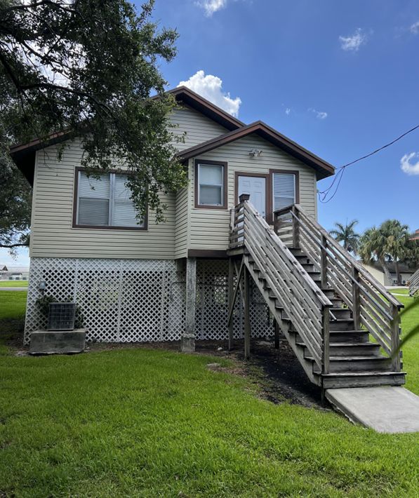House-like structure seemingly lifted above the ground with a staircase leading to the door and lattice fencing wrapping around the foundational structures below the house.